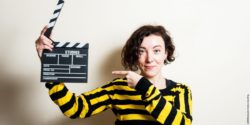 Photo: Young woman pointing on a clapperboard in her hand; Copyright: panthermedia.net/Fabiopagani