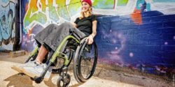 Photo: A young woman leans backwards with her wheelchair against a spray-painted wall; Copyright: MEYRA GmbH