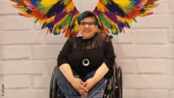 Miriam Langhoff poses laughing in front of the colorful wings in the BRSNW selfie spot at REHACARE 2024
