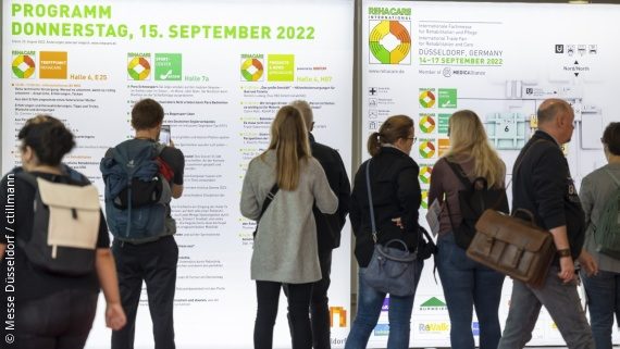 Photo: Several people stand in front of a wall with the forum programmes at REHACARE 2022; Copyright: Messe Düsseldorf / ctillmann
