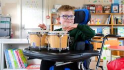 Child seated in a LECKEY BeMe pediatric seating system playing hand drums in a classroom