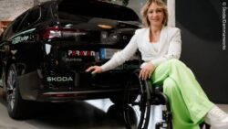 Kristina Vogel sits in a wheelchair next to the back of her black car; Coypright: Škoda/Dammanworks