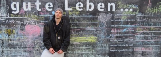 Photo: Janis Geiger in front of a wall with "the good life" written on it; Copyright: Janis Geiger