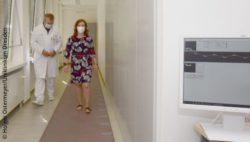 Photo: Patient Sabine H. walking down a corridor together with Prof. Tjalf Ziemssen; Copyright: Holger Ostermeyer/University Hospital Dresden