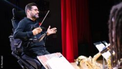 Wheelchair user conducting musicians with a baton on stage
