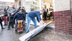 Photo: A shop owner who allows a wheelchair user access to his shop by means of a mobile ramp; Copyright: Jörg Farys | AG Urban