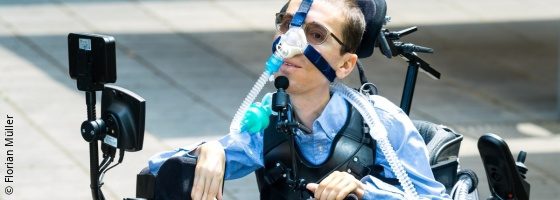 Photo: young man with glasses in an electric wheelchair connected to a ventilation system - Marcel Renz; Copyright: Florian Müller 