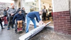 Photo: A shop owner who allows a wheelchair user access to his shop by means of a mobile ramp; Copyright: Jörg Farys | AG Urban
